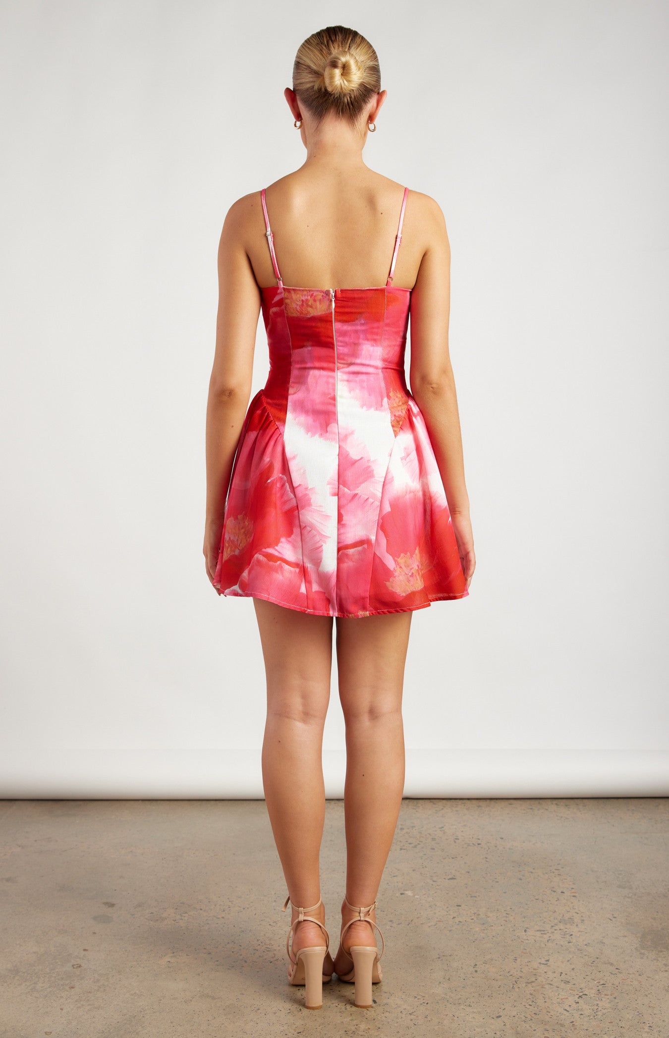 The coco dress is a vibrant and feminine mini dress featuring a striking pink and red floral pattern. It has a fitted bodice with a structured silhouette, accentuating the waist before flaring into a short, flouncy A-line skirt. The bodice is designed with delicate spaghetti straps, adding a touch of elegance and lightness to the overall look.
The neckline is slightly asymmetrical, with an angular panel that runs diagonally across the front, creating a unique and modern design element. The fabric a