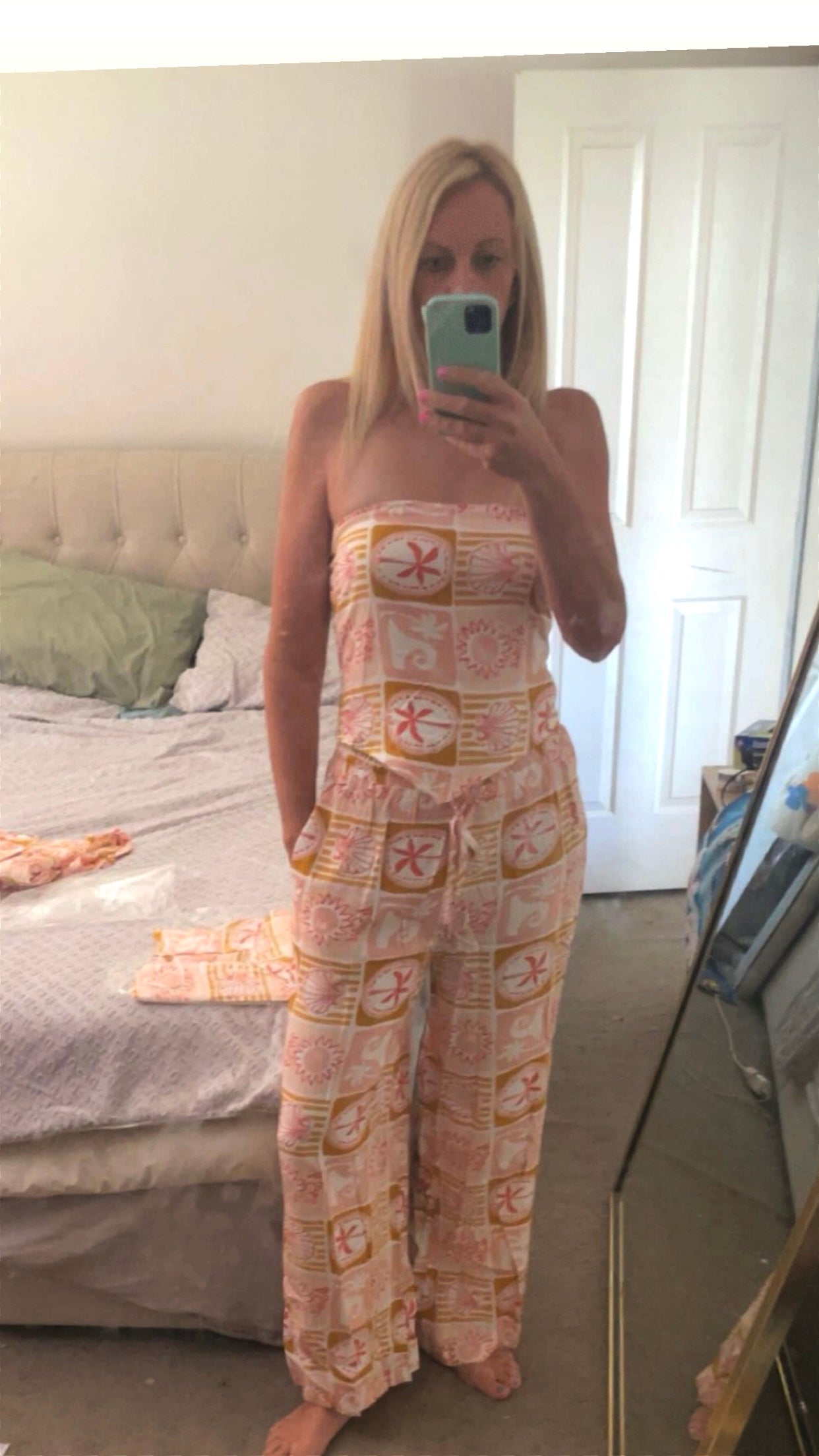 A vibrant two-piece set featuring a geometric design of colorful palm trees, waves, and sun in dreamy hues of blush, rose, rust, and yellow. The set includes elastic drawstring waist pants with pockets for effortless comfort, paired with a matching handkerchief-cut crop top. The top features an elasticized back for a flattering, fitted shape, making it the perfect blend of style and ease