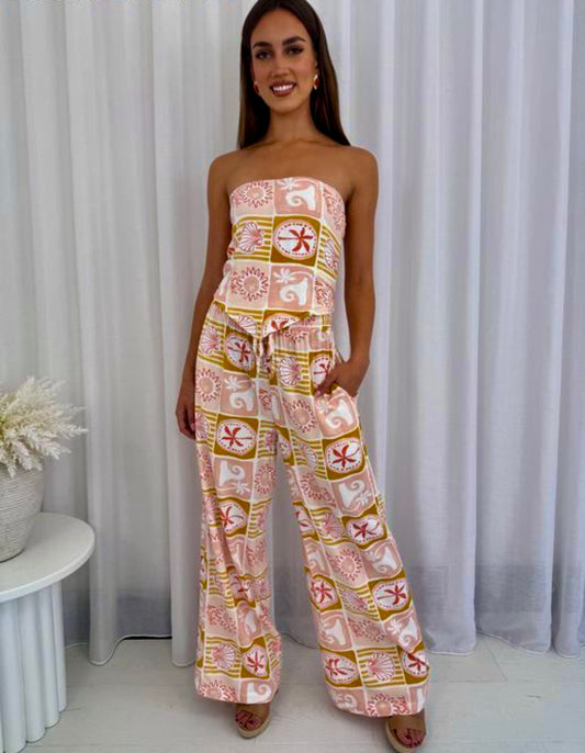 A vibrant two-piece set featuring a geometric design of colorful palm trees, waves, and sun in dreamy hues of blush, rose, rust, and yellow. The set includes elastic drawstring waist pants with pockets for effortless comfort, paired with a matching handkerchief-cut crop top. The top features an elasticized back for a flattering, fitted shape, making it the perfect blend of style and ease